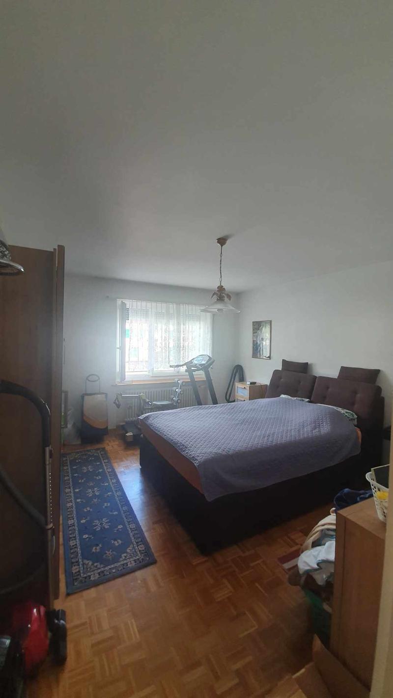 Bedroom with bed, window, radiator, treadmill, blue rug, picture, desk, bedheadboard, carpet, wooden floor