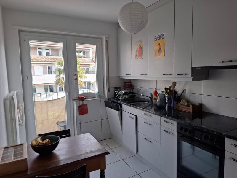 White cabinets, black countertop, black oven, wooden table, bananas in bowl, glass door