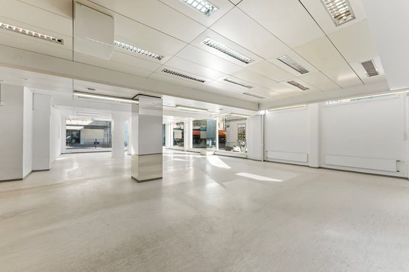 Empty room with white walls, white ceiling, white floor, central column, windows, and ceiling lights