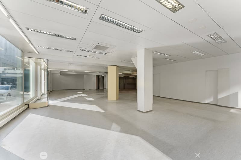 Empty room with white walls, ceiling, and floor, large windows, central column, and ceiling lights