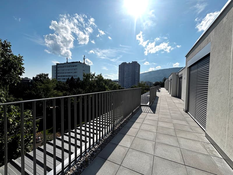 A balcony with a metal railing, tiled floor, and a view of the city and mountains.
