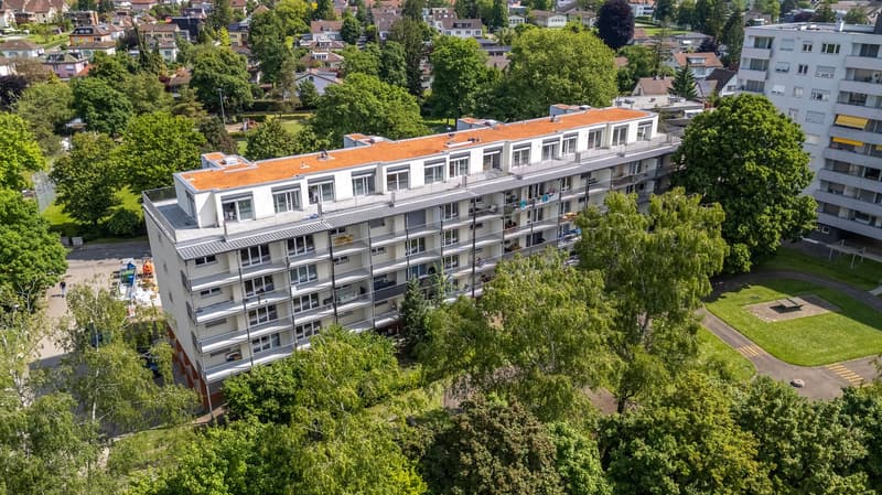 A multi-story building with multiple balconies, surrounded by trees and grass.
