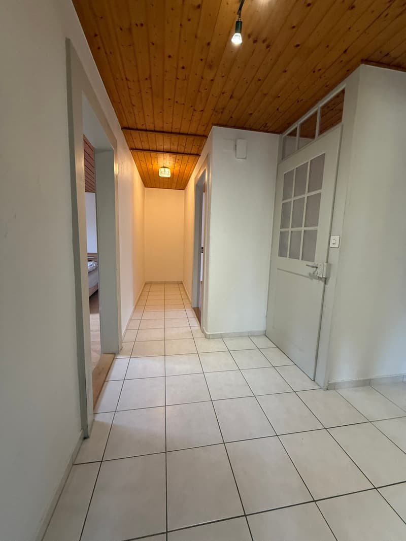 Empty hallway with white tiles, wooden ceiling, and two doors on either side.