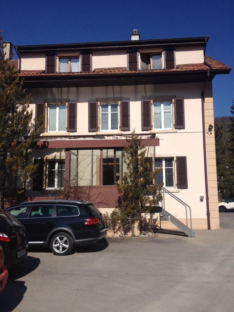 Two-story house with brown shutters, white windows, and a red roof. A black car is parked in front.
