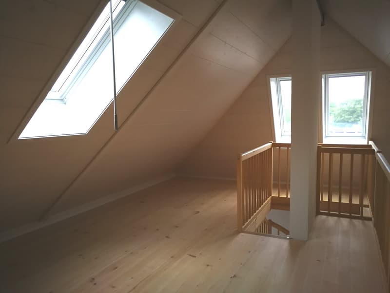 Empty attic room with wooden floors, two windows, and a wooden staircase.