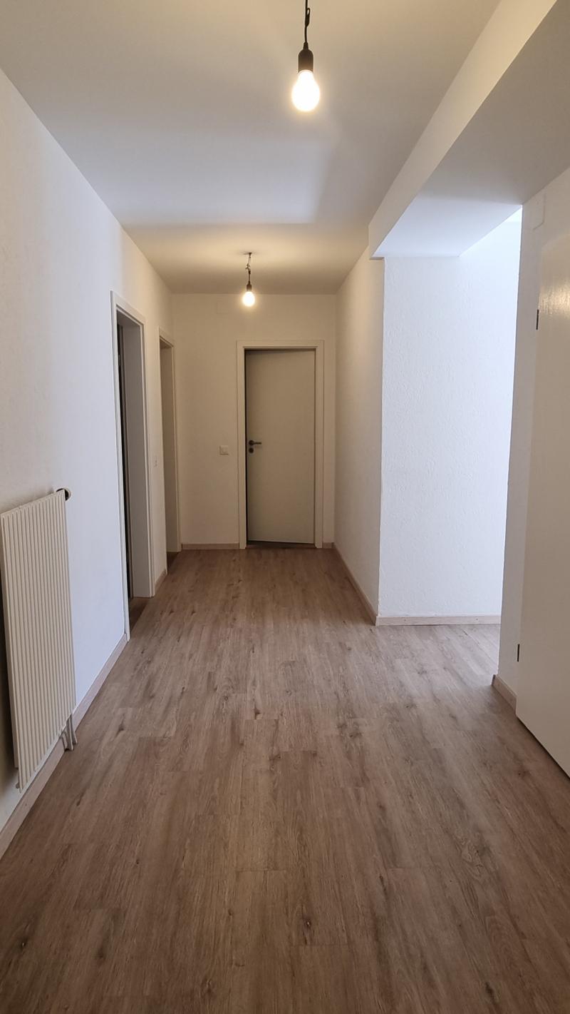 Empty room with wooden floor, white walls, two doors, and ceiling lights