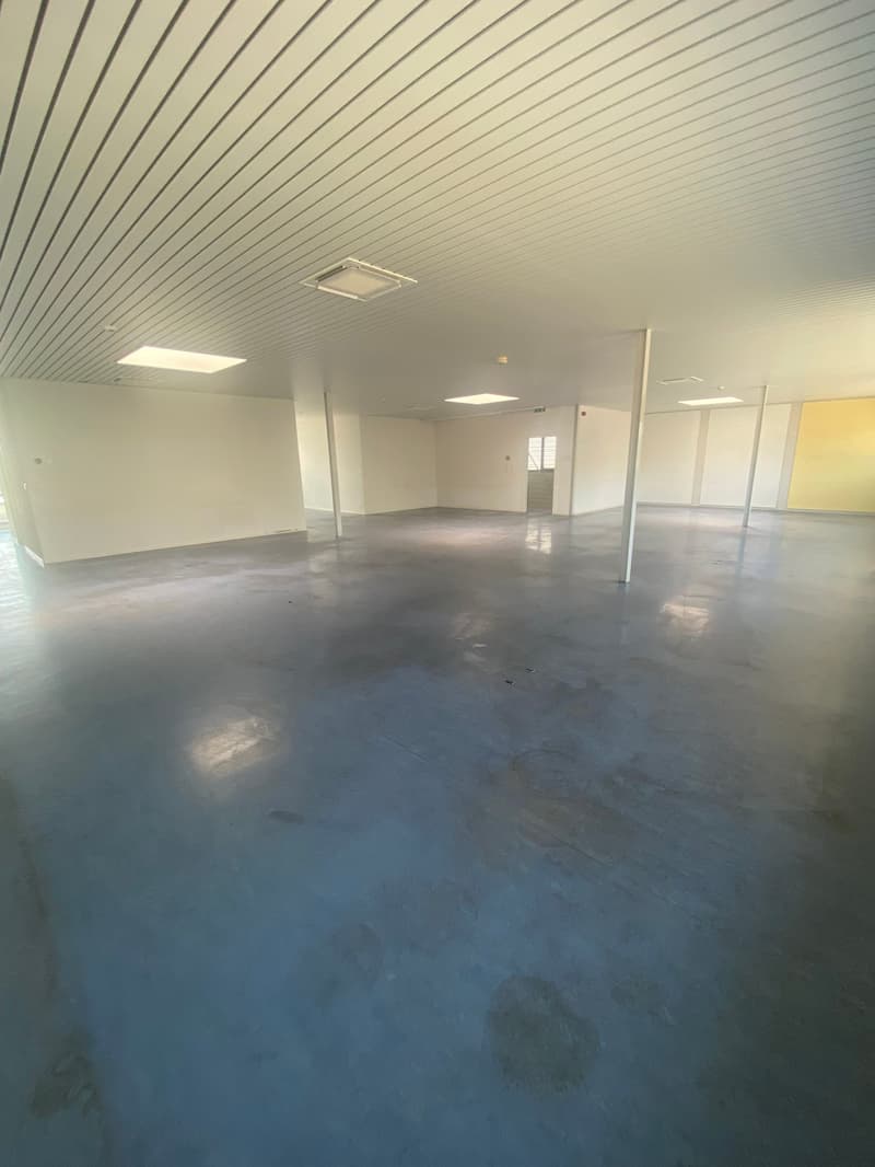 spacious room with a white wall, ceiling, and floor. A white-colored pipe is installed on the ceiling, and a yellow-colored partition is on the right side. On the left side, a window is located.