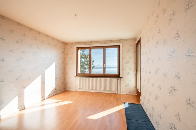 Empty room with wooden floors, flower-printed wallpaper, large window with view of the lake
