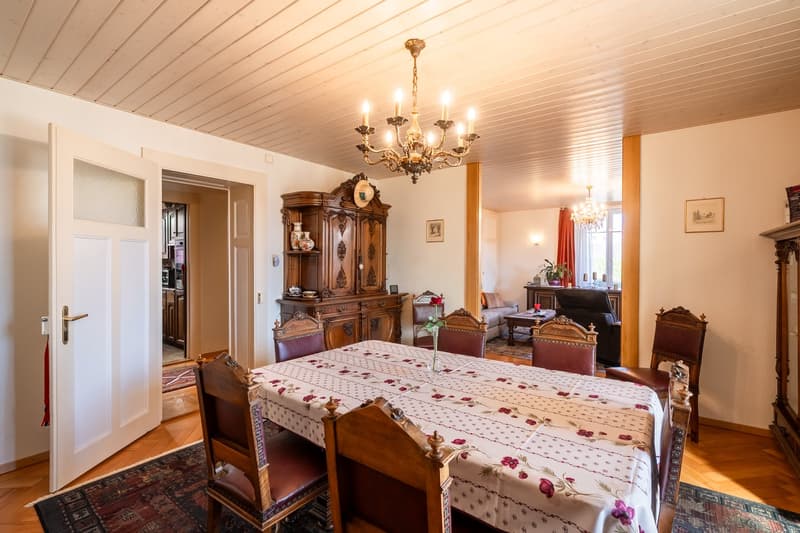 Dining room with table and chairs, chandelier, large cabinet, coffee table, armchair, sofa, flower vase, carpet, picture frames, cabinet