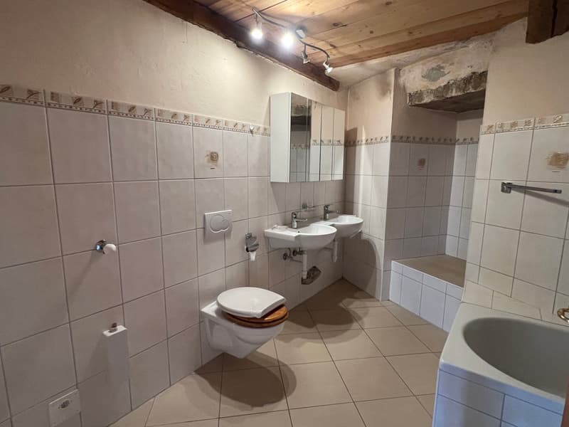 Tiled bathroom with two sinks, toilet, and storage cabinets. Exposed wooden beams on the ceiling.