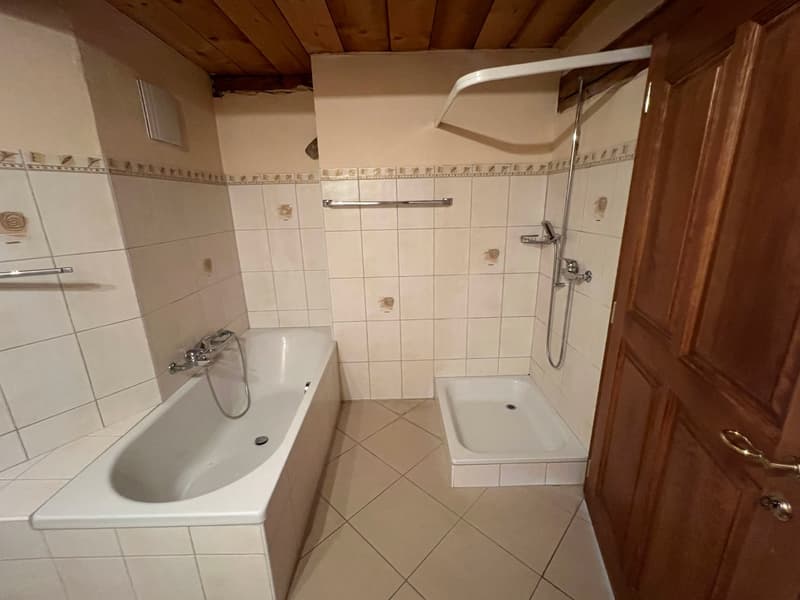 Tiled bathroom with a bathtub, shower, and vanity sink. The ceiling has exposed wooden beams.