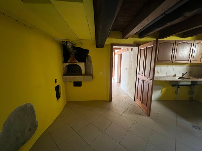 The image shows a kitchen area with a fireplace, wooden cabinets, and tile flooring. The walls are painted in a bright yellow color, creating a warm and cozy atmosphere. The room has an open layout, with a doorway leading to another part of the space.