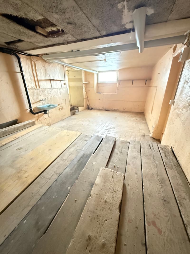 Empty room with wooden floor, sink, window, pipes on ceiling
