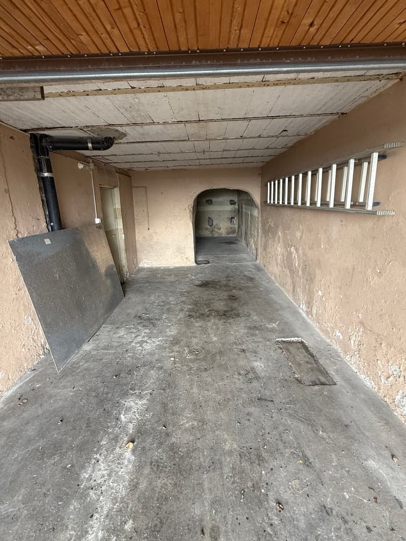Empty garage with concrete floor, wooden ceiling, and walls with visible damage and stains