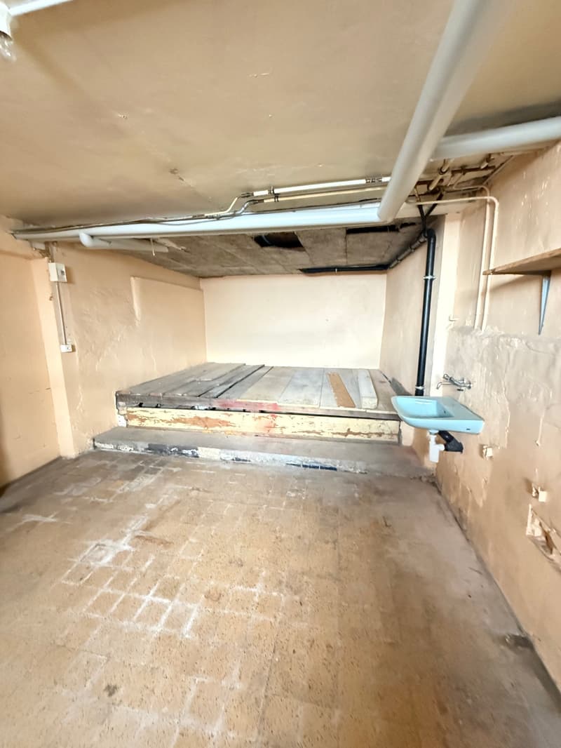 Empty room with concrete floor, wooden platform, sink, pipes, and electrical outlets