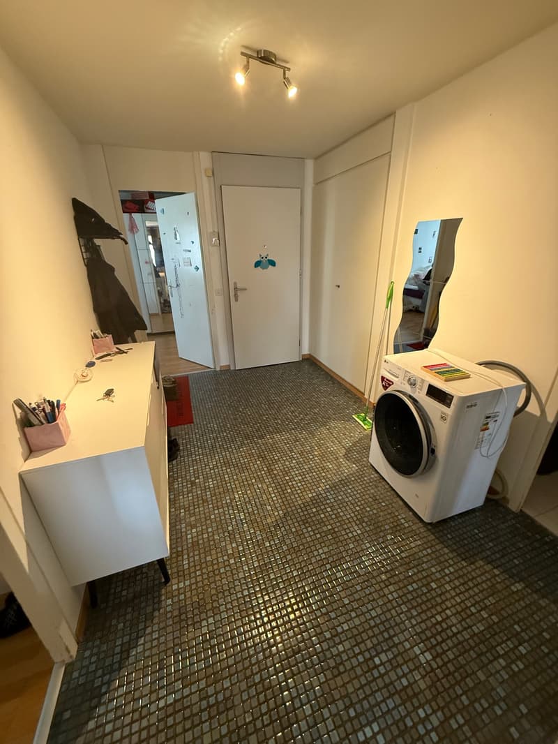 A small room with a white washing machine, a white cabinet, and a mirror on the wall.