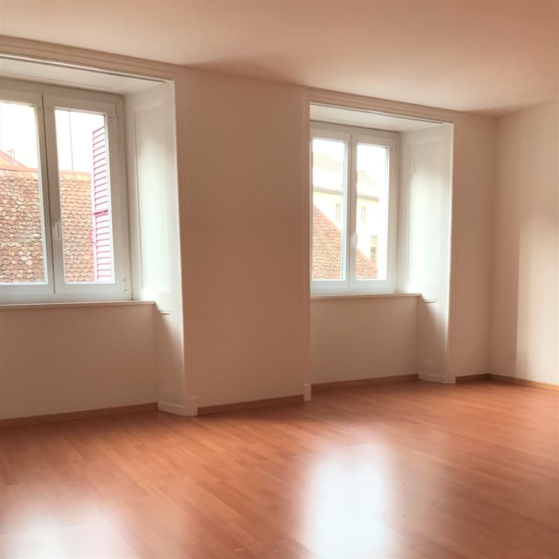 Empty room, wooden floor, white walls, two windows, view of the outside