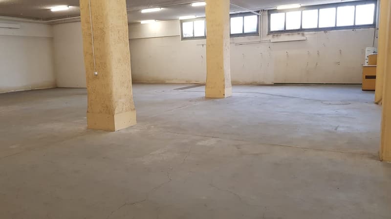 Empty room, white walls, concrete floor, support columns, lights on ceiling, windows on side wall