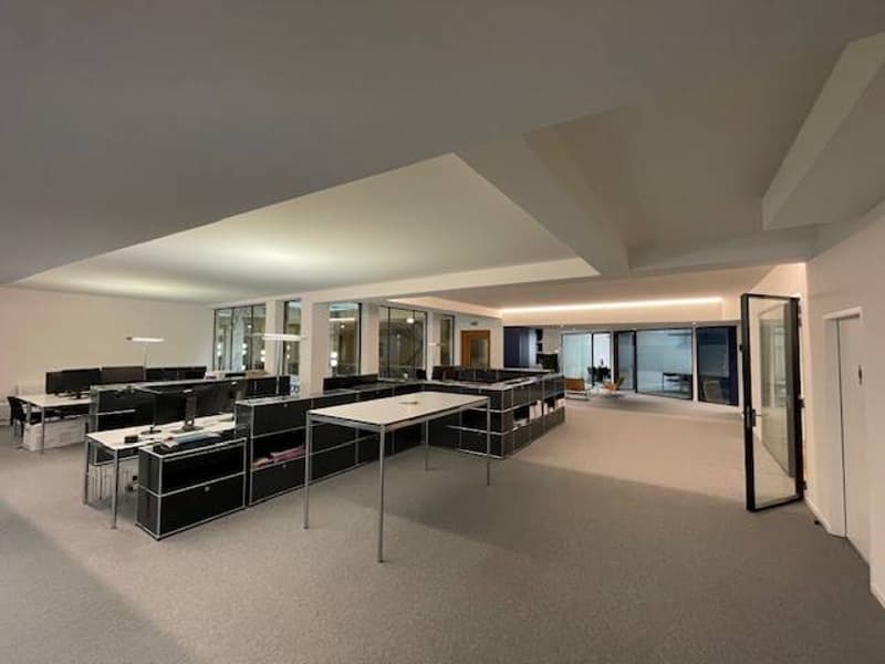 Spacious office space with glass walls, grey carpet, large tables and chairs, and desk lamp