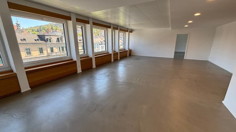 Empty room, concrete floor, large windows, wooden window sills, white walls, ceiling lights