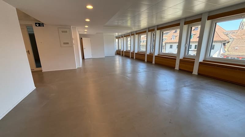 Empty room, concrete floor, white walls, large windows, wooden window sills, ceiling lights