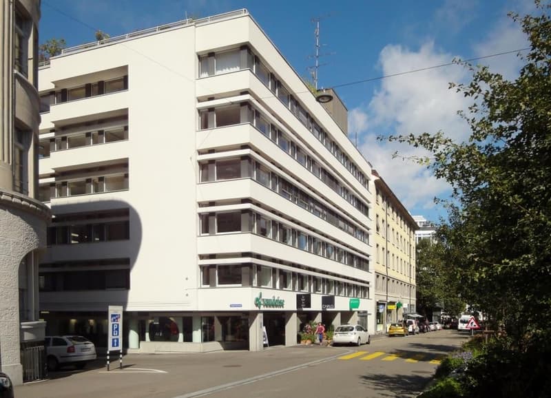 6 story building, white exterior, large windows, parked cars, storefronts, trees, street lights, street