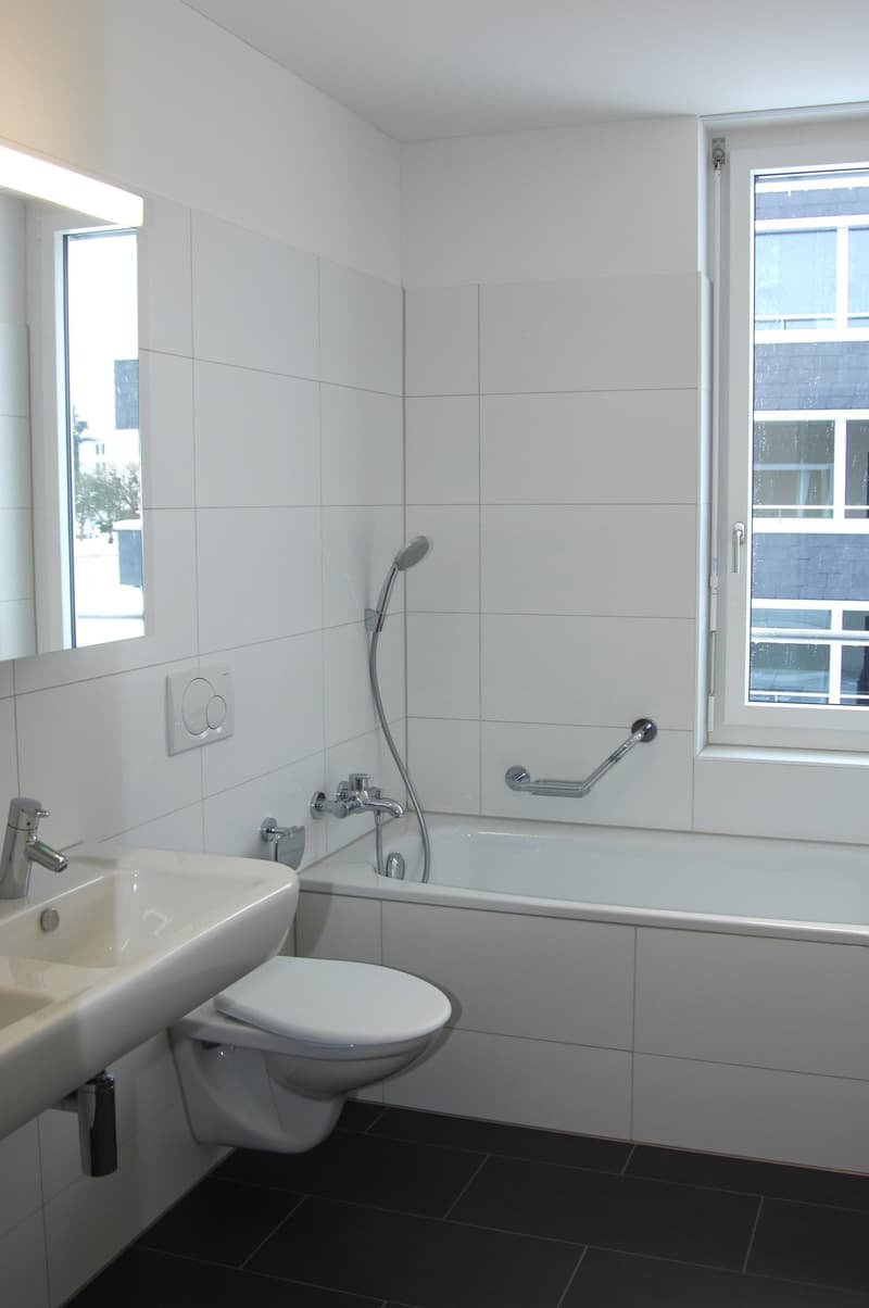 Bathroom with white tiles, white bathtub, white sink, white toilet, silver faucet, silver shower head, mirror, window