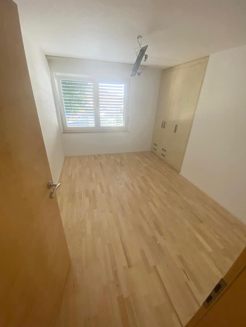 Empty room with wooden floor, built-in wardrobe, ceiling lamp, window with blinds.