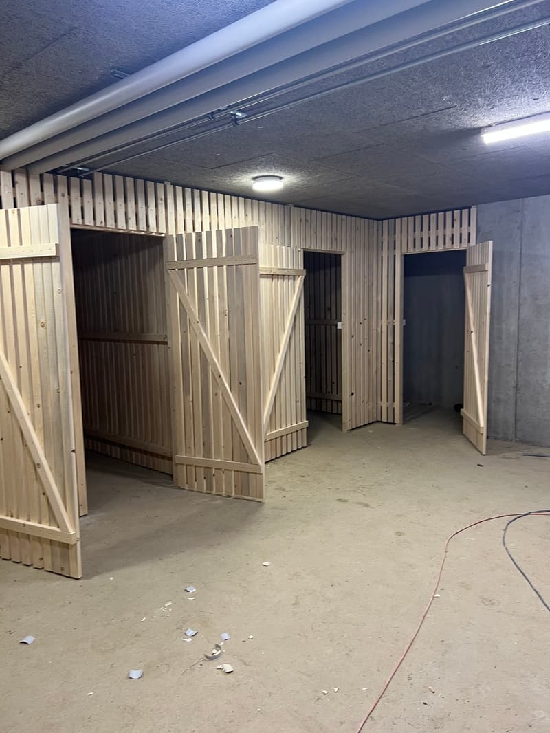 An empty, unfinished basement with wooden partitions, metal ceilings, and exposed wiring