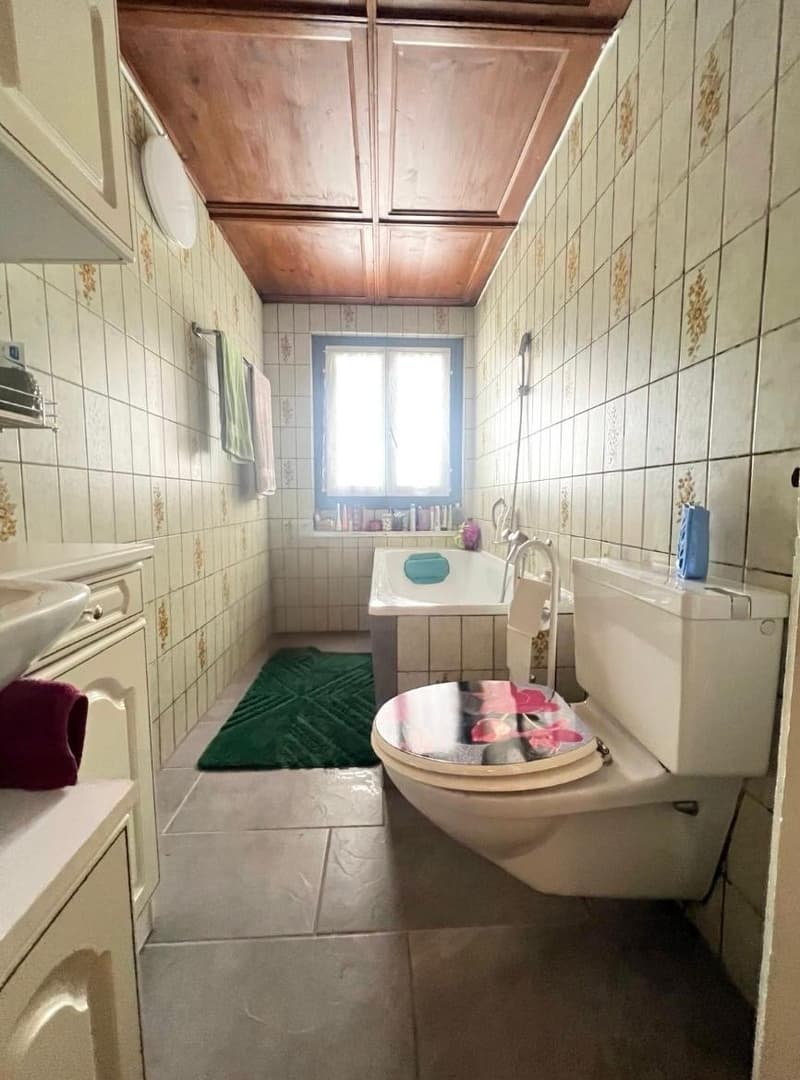 Bathroom with white walls, bathtub, toilet, sink, wooden ceiling, white tile flooring