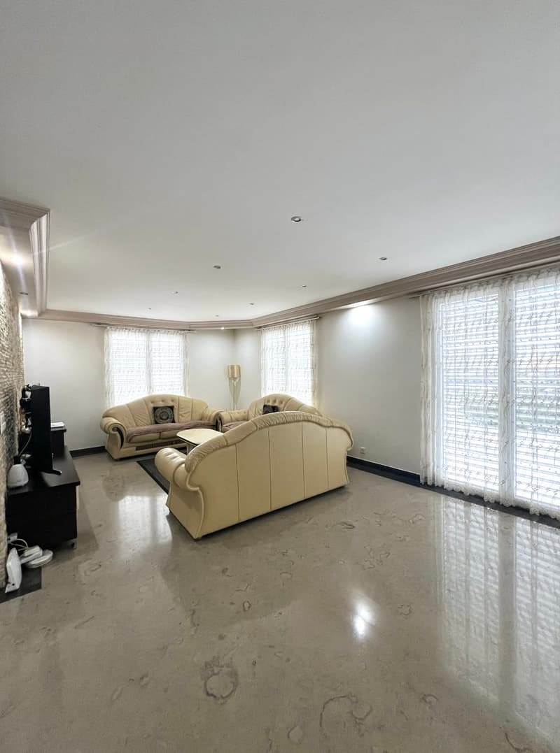 spacious living room, beige leather sofas, coffee table, TV, floor lamp, large windows, marble floor