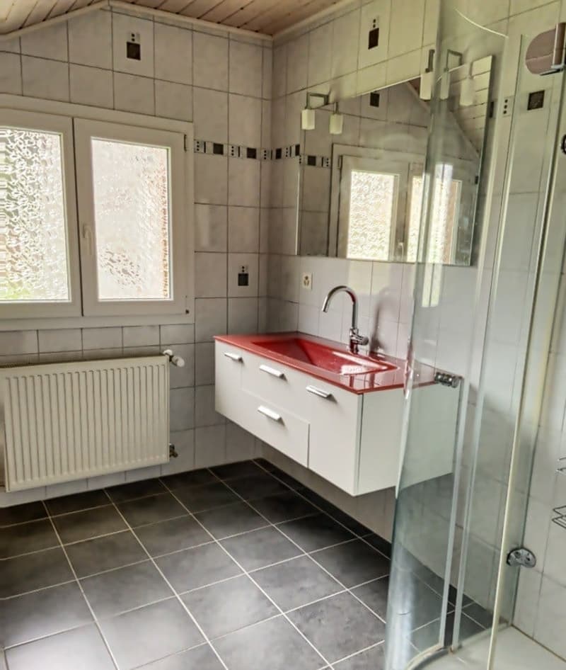 Bathroom with white tiles, red sink, white cabinets, glass shower enclosure, white radiator, mirror