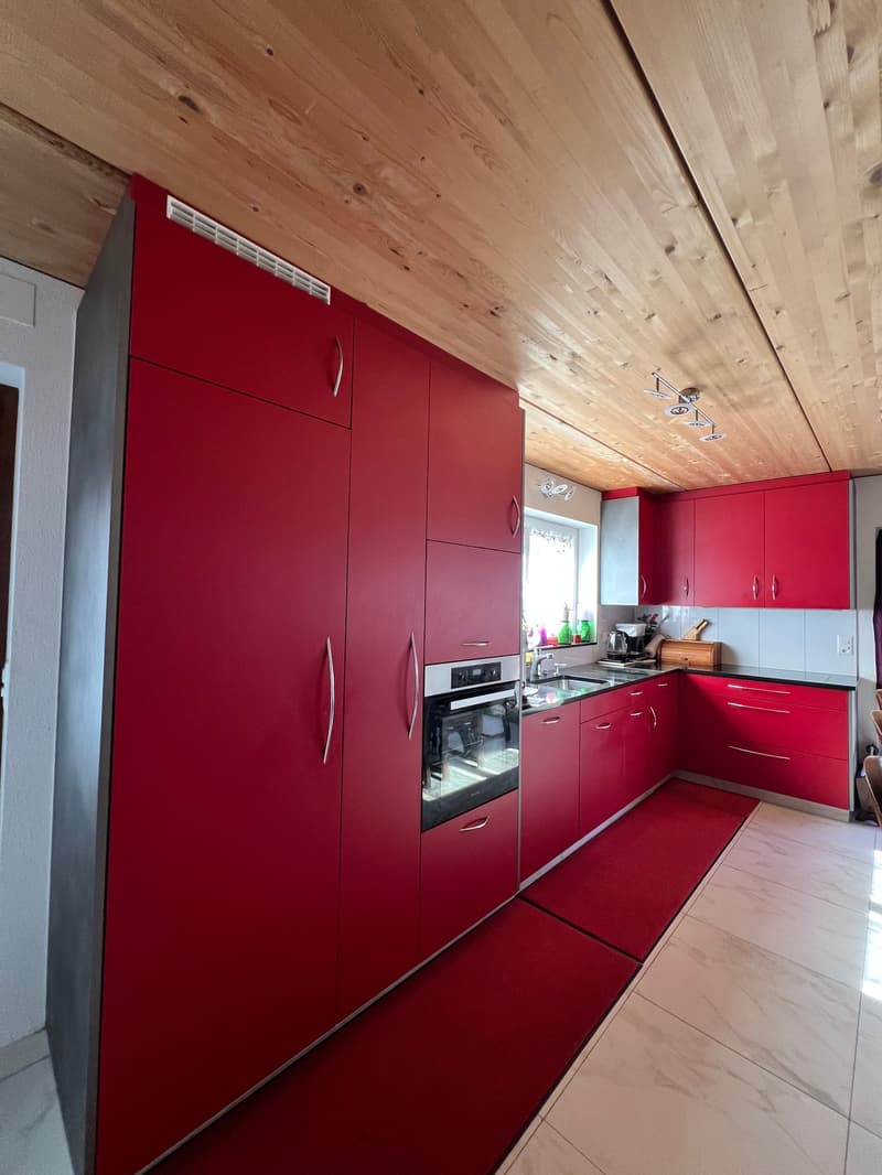 modern kitchen with red cabinets, wooden ceiling, white tiled floor, stainless steel oven, sink, countertop, red rugs