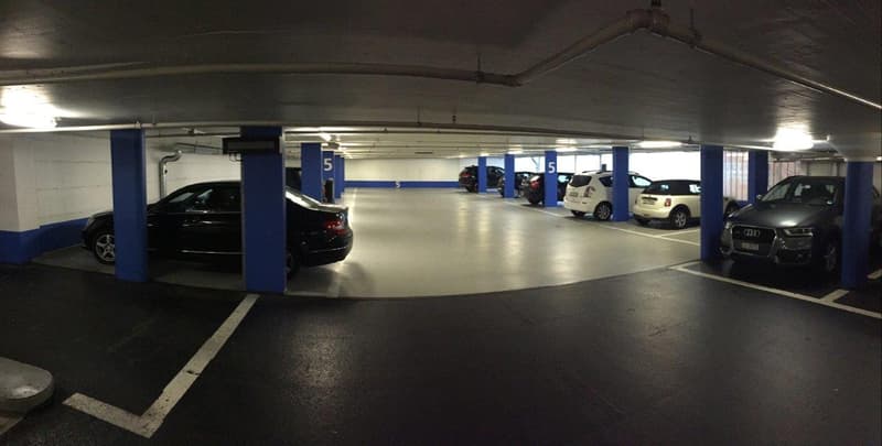 underground parking lot with several cars parked, blue pillars, white markings, ceiling lights