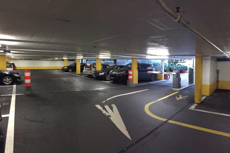 underground parking lot with several cars parked, yellow and white markings, pillars, and a barrier