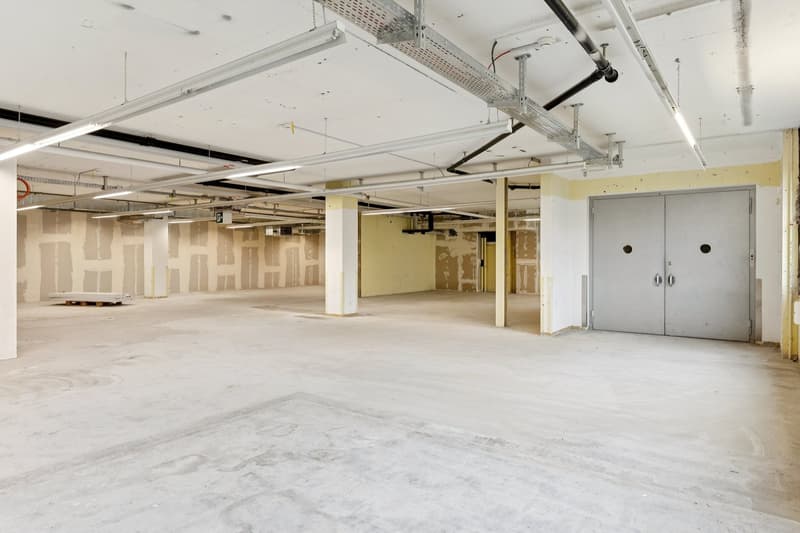 industrial style room with exposed pipes, unfinished walls, concrete floor, large windows, and a steel beam ceiling