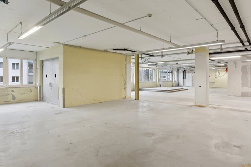 Empty room with concrete floor, white walls, and exposed pipes and beams on the ceiling.