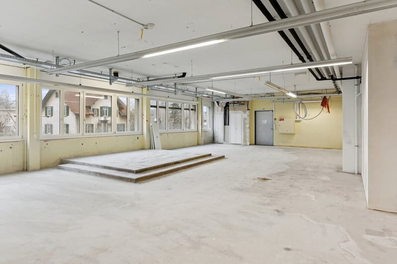 Empty room with concrete floor, large windows, raised ground floor, unfinished walls