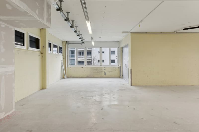 Empty room with white walls, concrete floor, windows, and doors.
