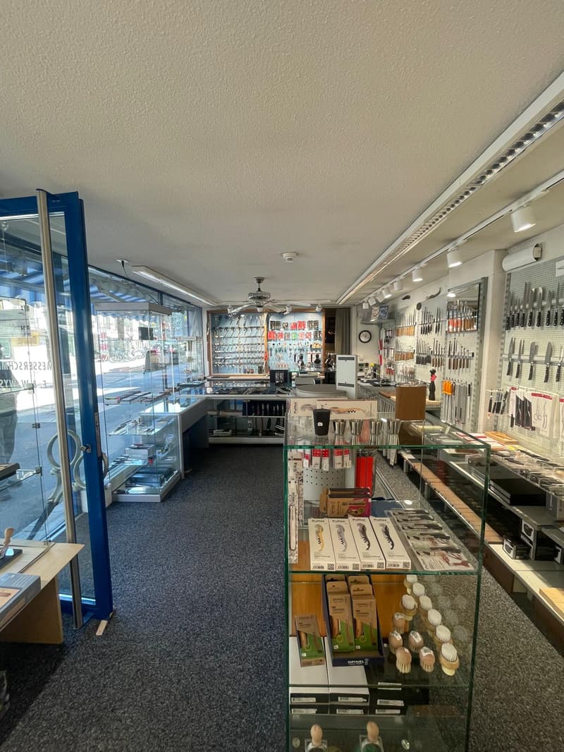 Empty store with glass walls, ceiling fan, shelves with products, and a counter.