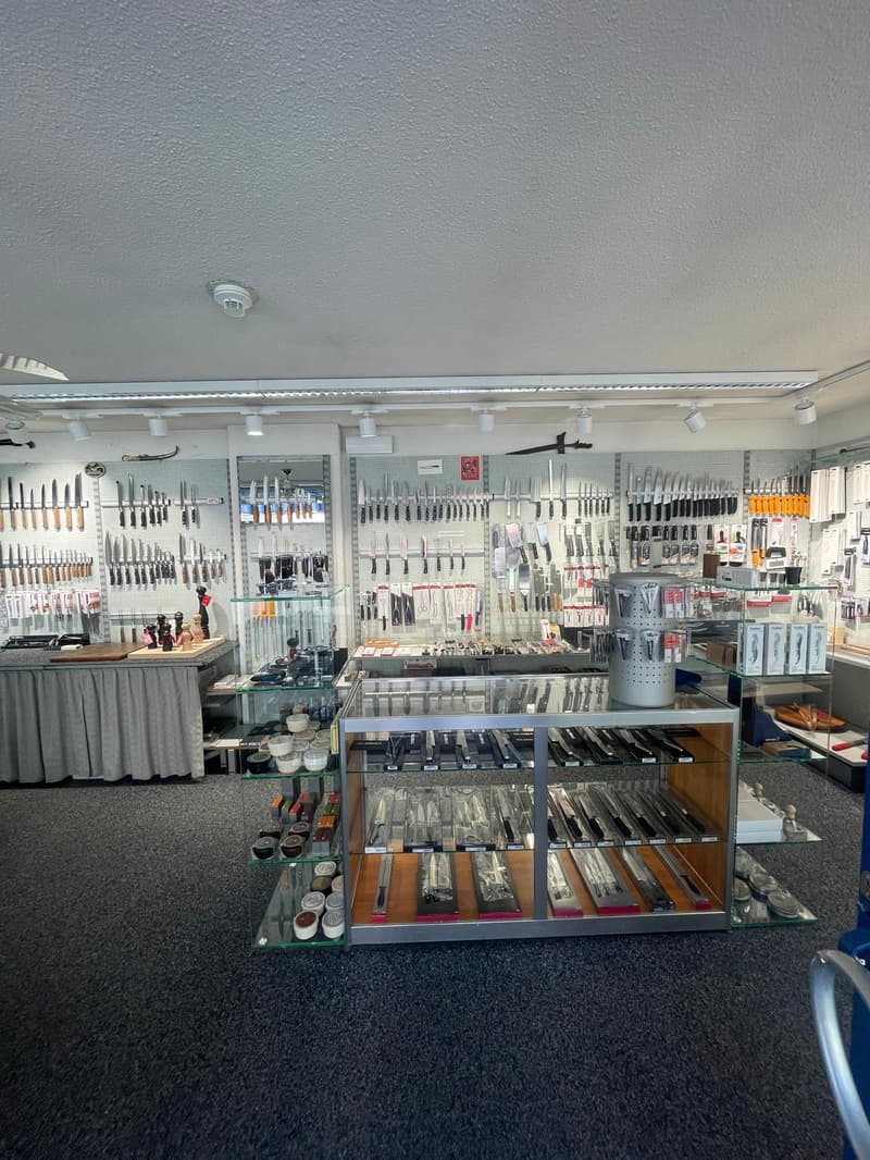 A store with a variety of knives and kitchen utensils on display, glass shelves, and a carpeted floor.