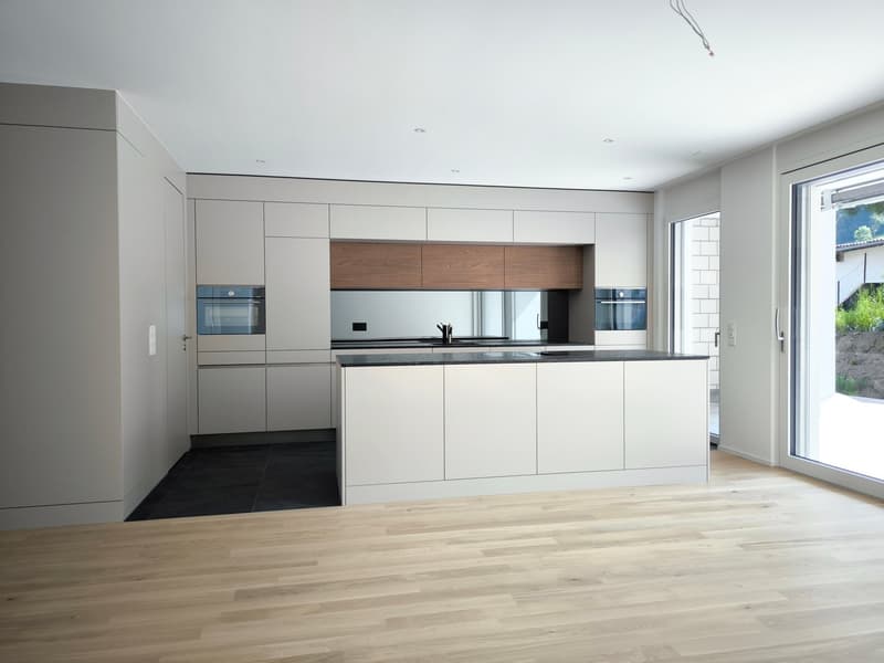 Modern kitchen with white cabinets, black countertops, and wooden island. Integrated appliances and large windows.