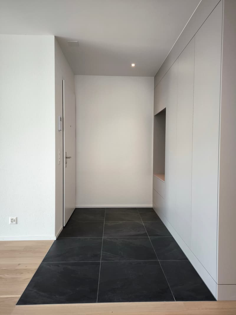 Empty room with white walls, black tiled floor, and built-in white cabinets.