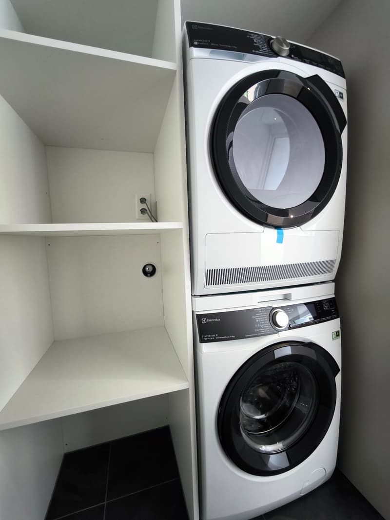 A white shelf with an outlet and a stack of a washing machine and dryer.