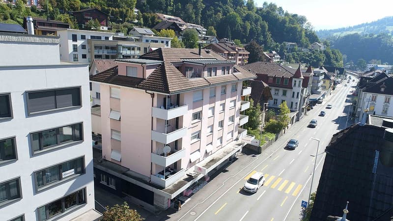 Aerial view of a multi-story residential building with several windows, balconies, and a street in front.