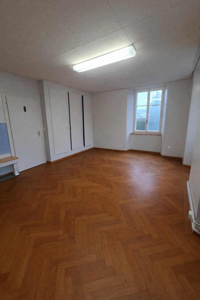 Empty room with wooden floor, white walls, single door, and a window with a view outside.