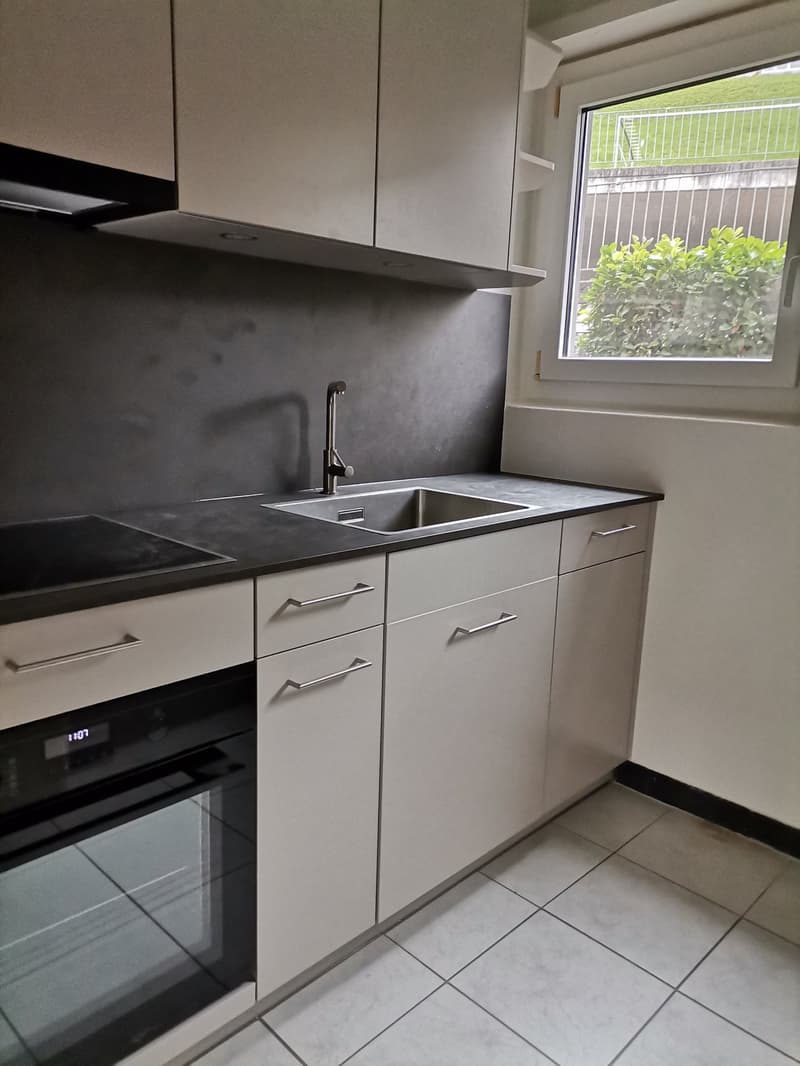 modern kitchen with white cabinets, black countertops, stainless steel sink, oven, and window with view