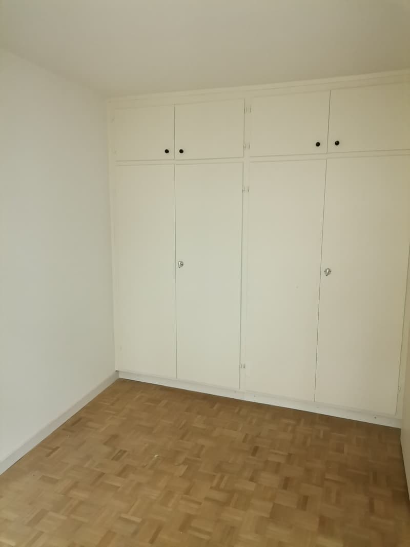 Empty room with wooden floor, white walls, and built-in wardrobes