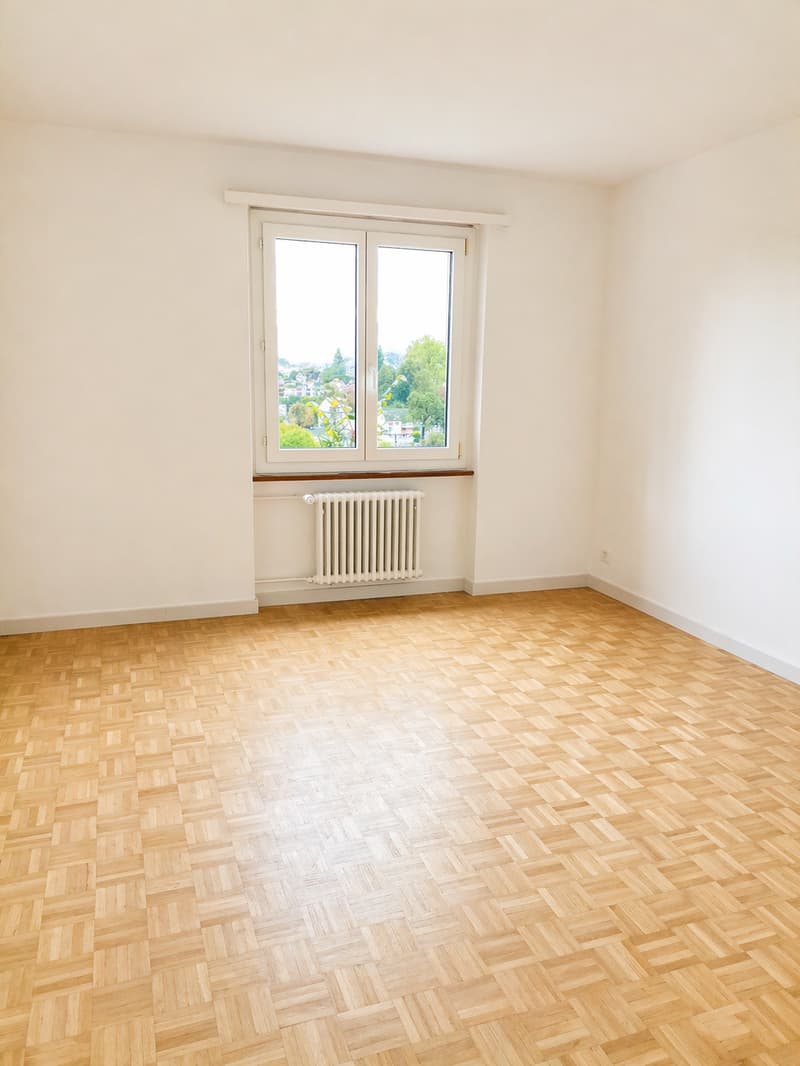 empty room, wooden parquet floor, white walls, large window, white radiator