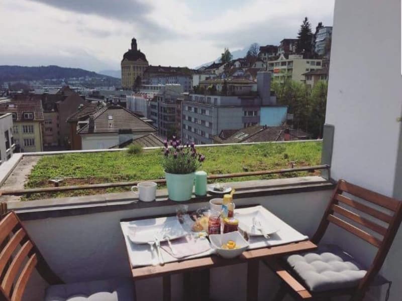 Balcony with table and chairs, green plants, city view, breakfast items